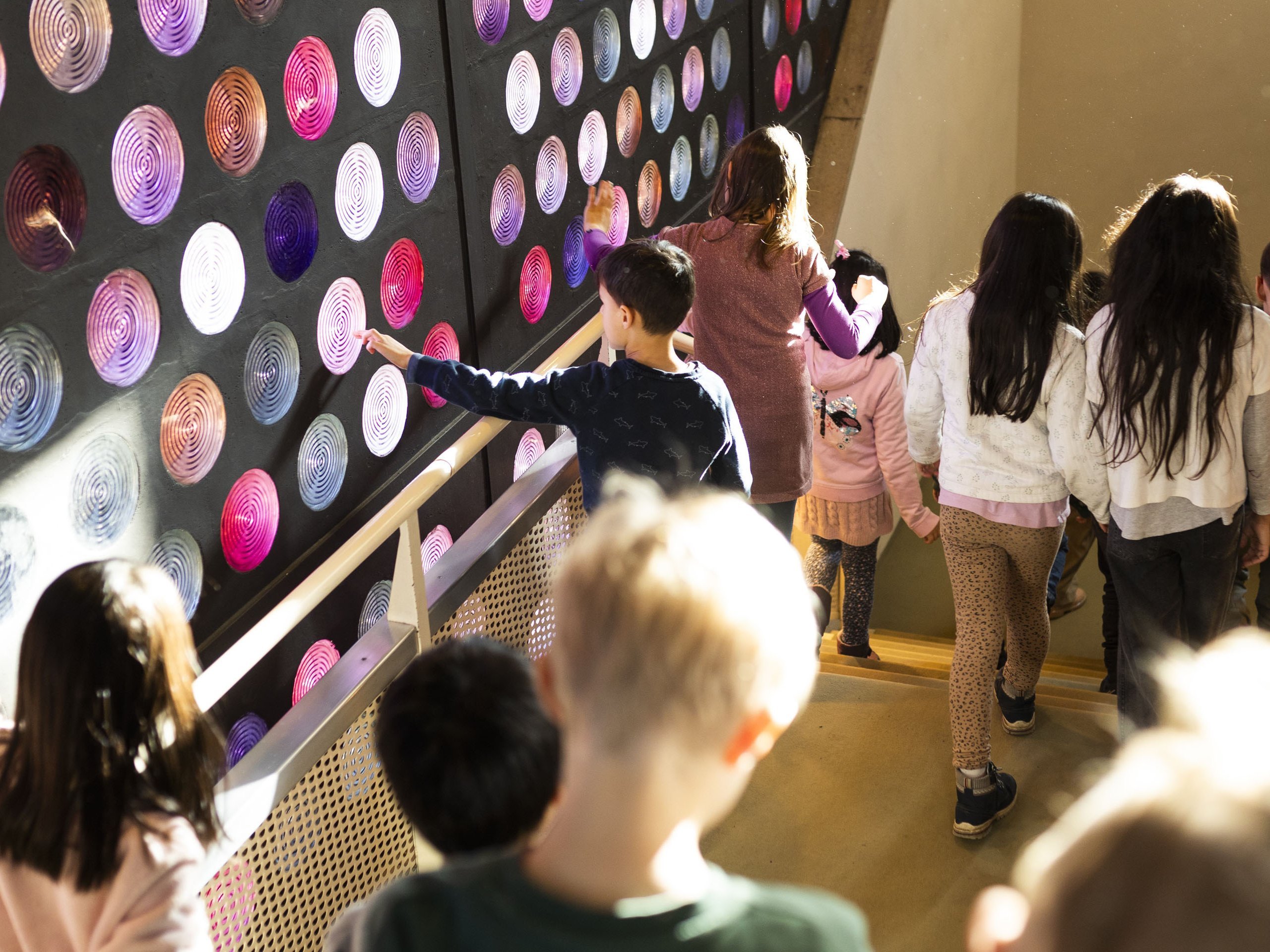 Kinder gehen an bunte Glassteinen in der Philharmonie entlang